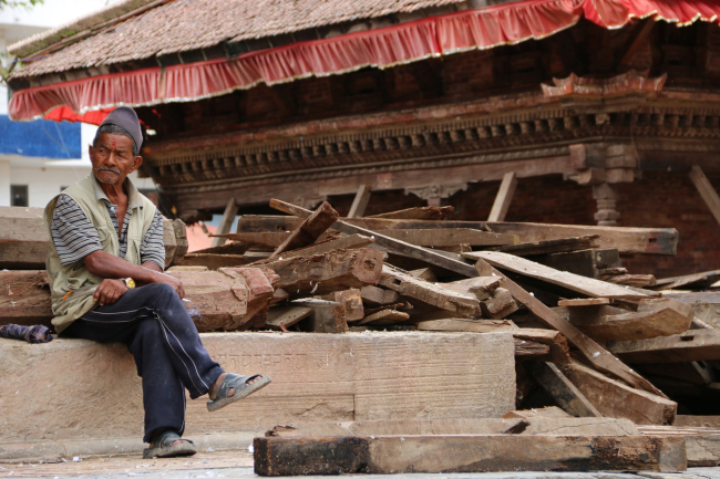 Местный житель рядом со спасенными деревянными фрагментами зданий на площади Дурбар (г. Катманду) © Kai Weise