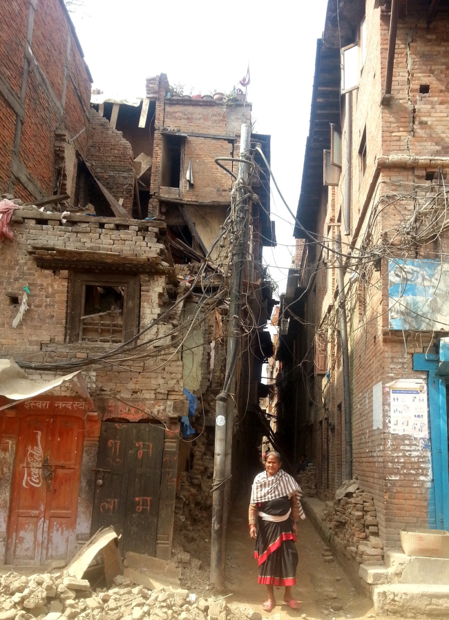 A woman in traditional attire standing in front of an area of historic Bhaktapur which badly damaged.  Kai Weise